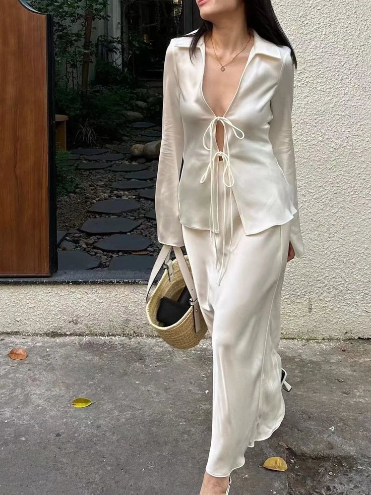 Woman in a white satin top and long skirt with a straw bag outdoors