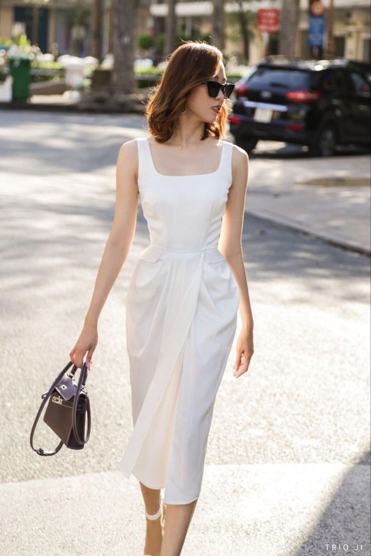 Woman in a white dress and sunglasses walking on a street