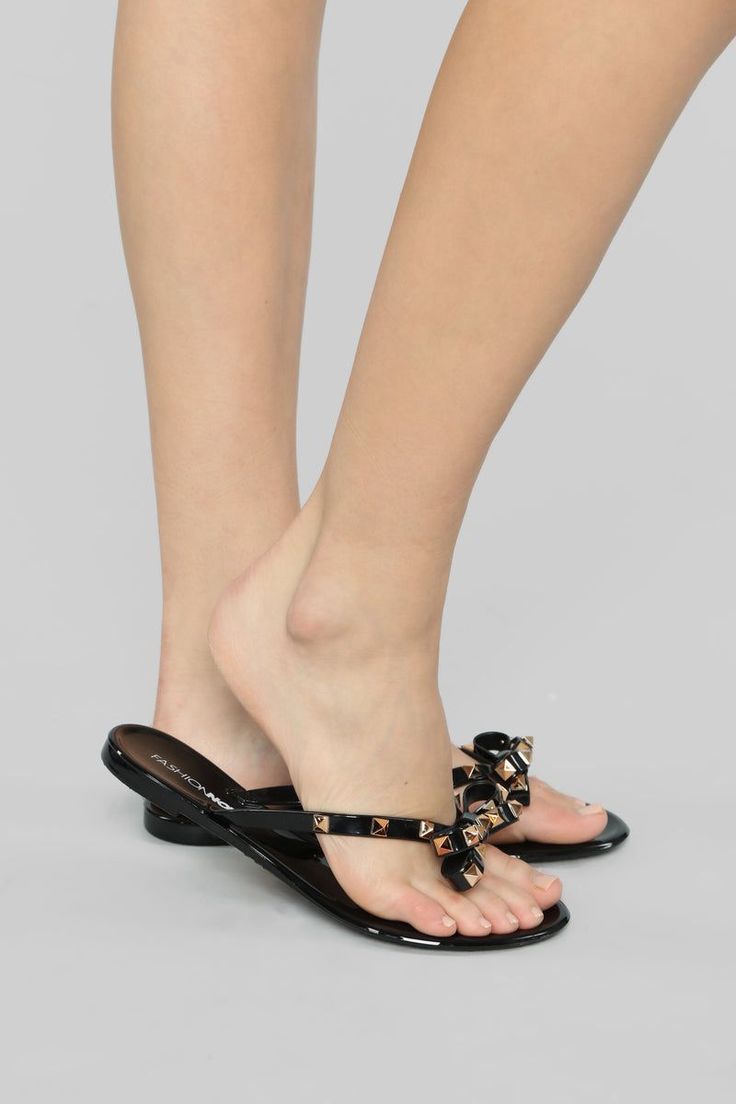 Person wearing black flip flops with studded bows on a light background