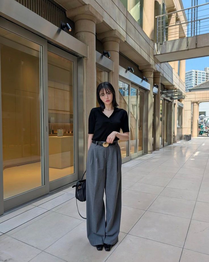 Woman with short hair and glasses wearing a black top and wide leg pants outdoors
