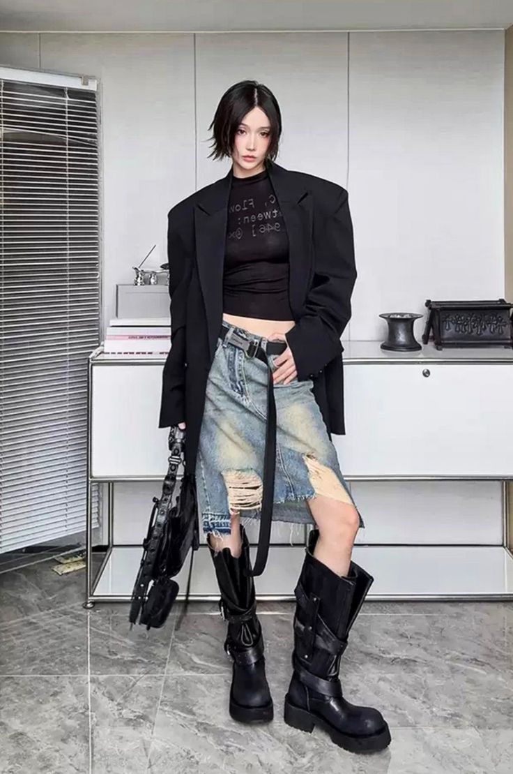 Woman with short black hair wearing a blazer, crop top, ripped denim skirt, and tall boots