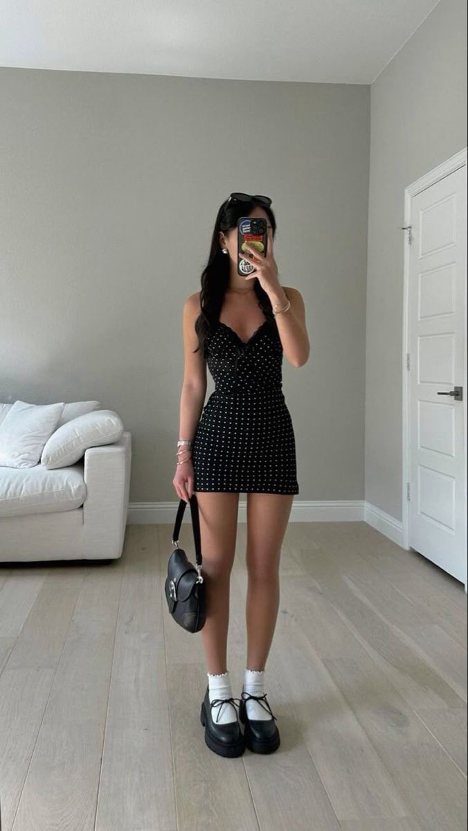 Woman in a black polka dot dress holding a handbag indoors