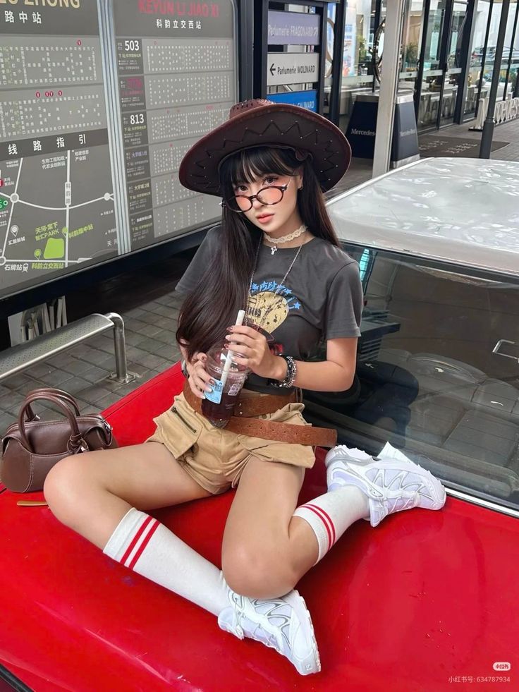 Woman in a cowboy hat and khaki shorts sitting on a red car outdoors