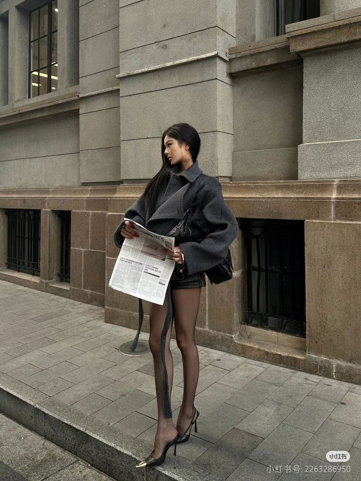 Woman in an oversized jacket, leather shorts, and sheer tights on a city street