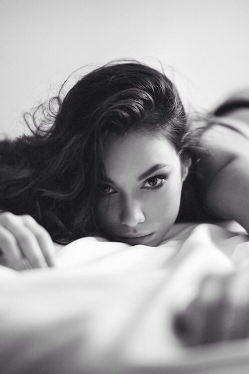 Woman with long hair lying on a bed in a provocative pose, black and white