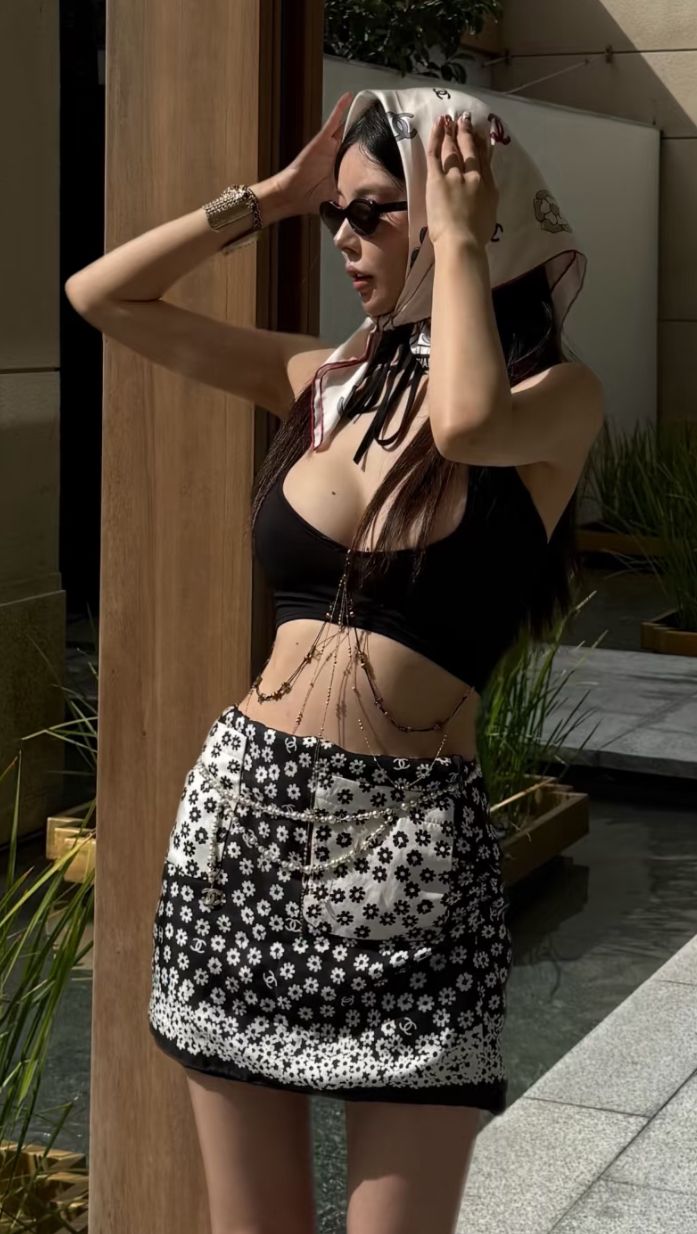 Woman in a black crop top and floral mini skirt with a head scarf and sunglasses
