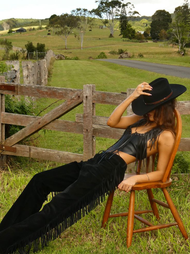 Woman in a cowboy hat and fringe outfit posing on a chair in the countryside