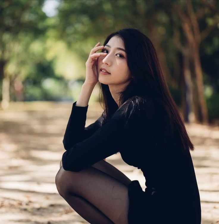 Woman with long black hair in a black dress squatting outdoors