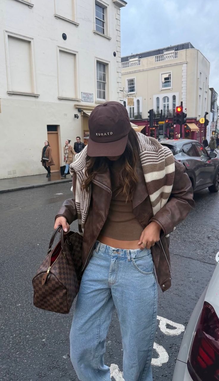 Person in a brown leather jacket and light wash jeans on a street