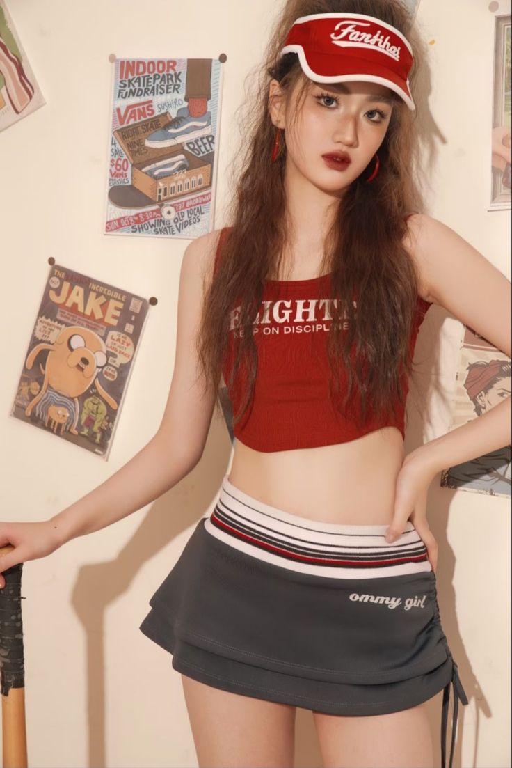 Woman in a red crop top and mini skirt with a red visor indoors
