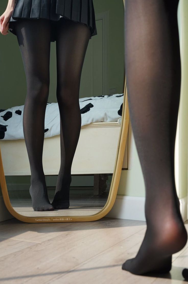 Person in a black pleated skirt and tights looking in a mirror