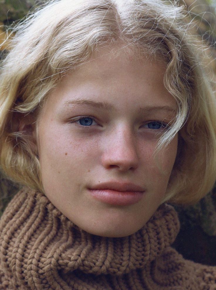 Close up portrait of a young person with blonde hair and blue eyes wearing a turtleneck sweater