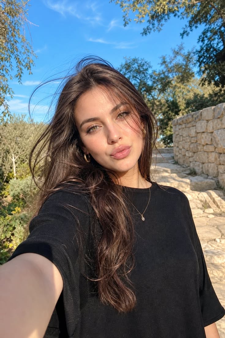 Woman with long brown hair wearing a black shirt outdoors under a blue sky