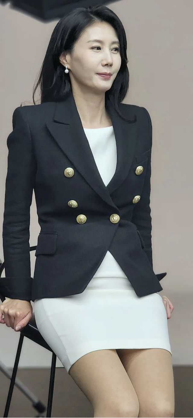 Woman in a black blazer and white skirt with long dark hair