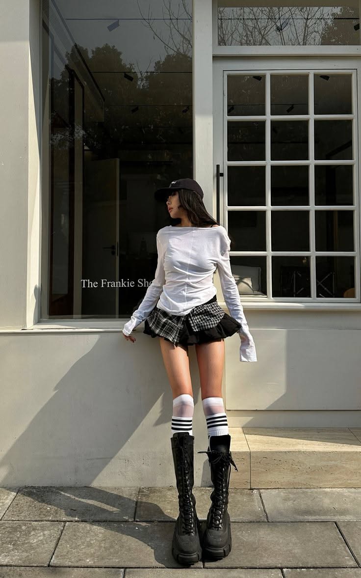 Woman in a plaid skirt and long boots posing outdoors