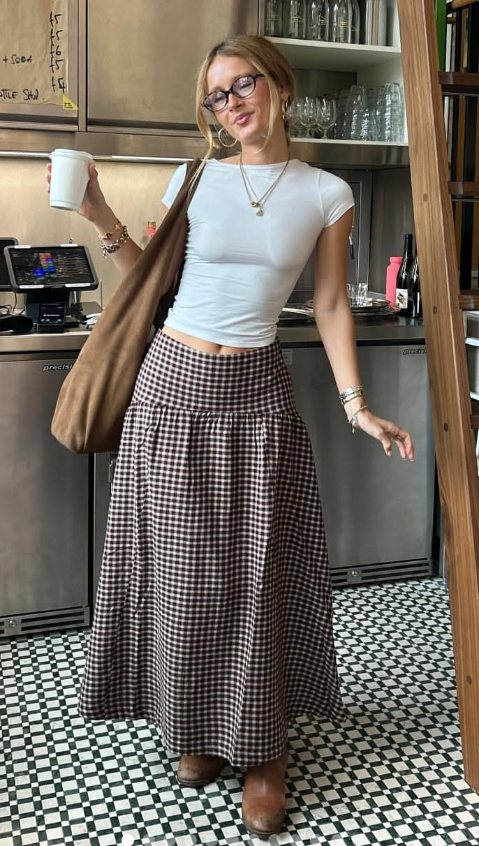 Woman in a white top and plaid skirt holding a cup indoors