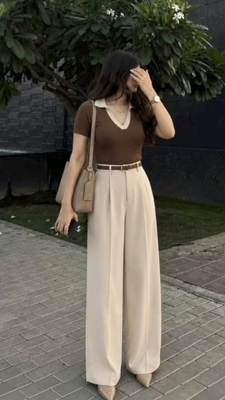 Woman in a brown polo shirt and wide leg pants holding a phone outdoors