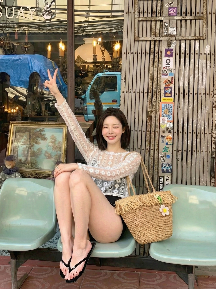 Woman in a lace top and black shorts sitting outdoors with a straw bag
