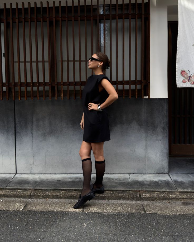 Woman in a black dress and knee-high socks standing on a street