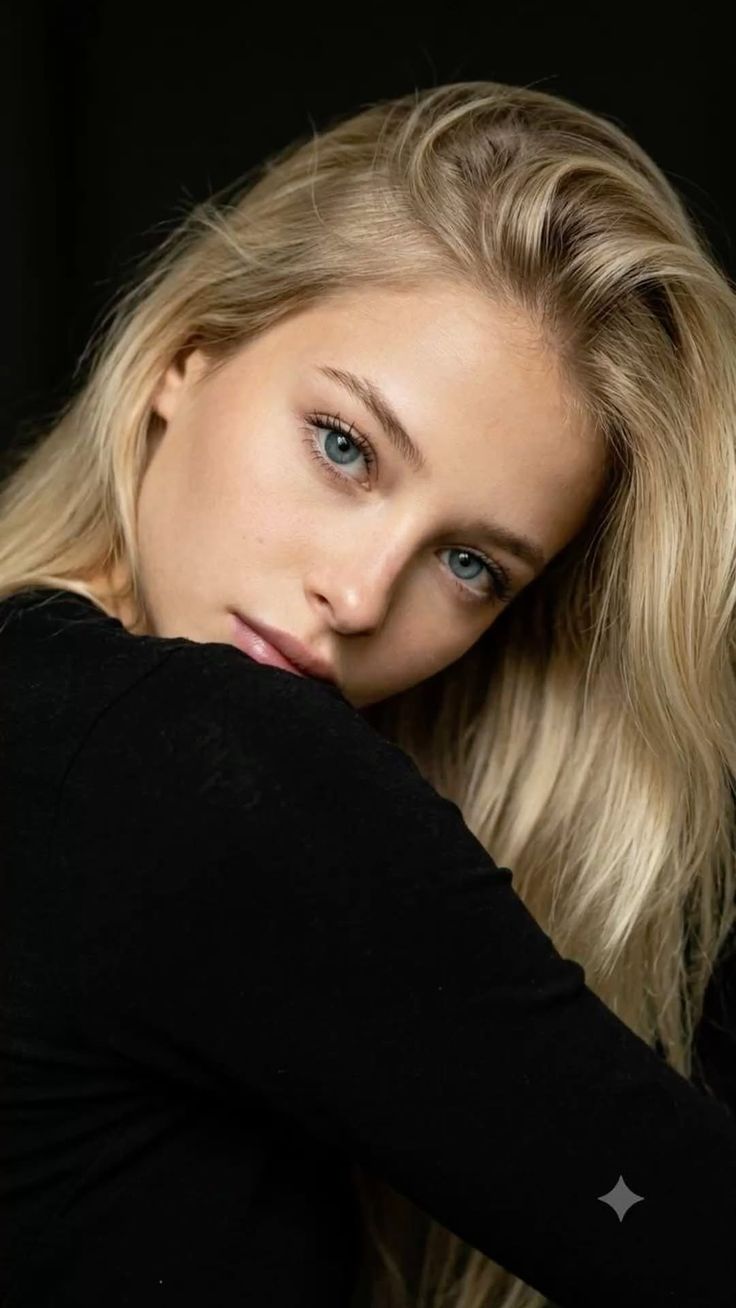 Woman with blonde hair and blue eyes wearing a black top, looking at the camera