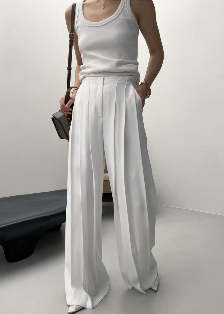 Person in a white tank top and wide leg pants holding a shoulder bag