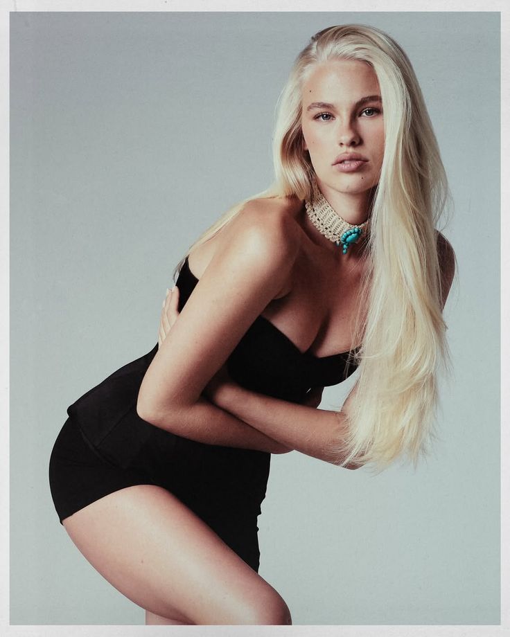 Woman with long blonde hair in a black dress and choker posing in a studio