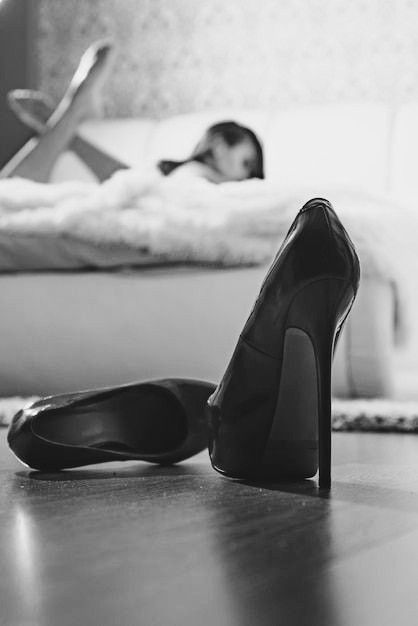 High heels on the floor with a person in bed in the background
