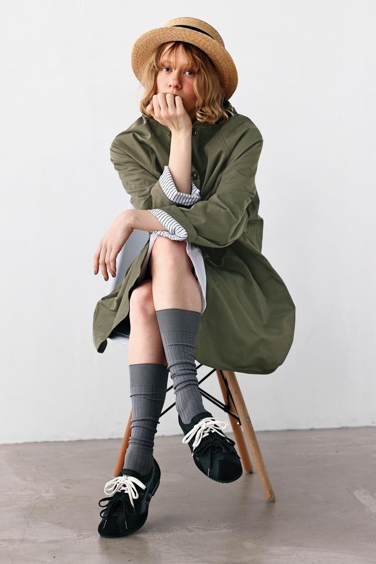 Person in a straw hat and green jacket sitting on a chair indoors