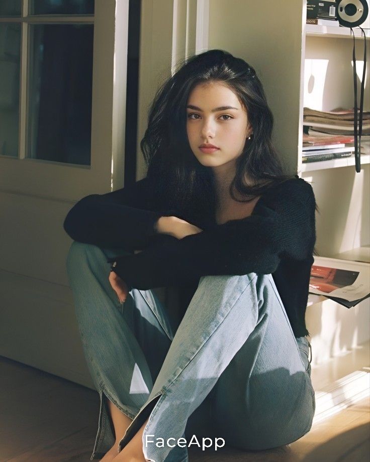 Young woman with long dark hair sitting on the floor in soft indoor lighting