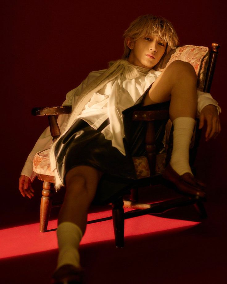 Person with blonde hair in a white shirt and dark shorts sitting on a chair