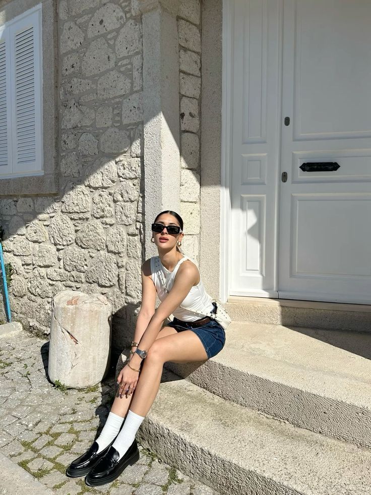 Woman in a denim skirt and white tank top sitting on stone steps outdoors