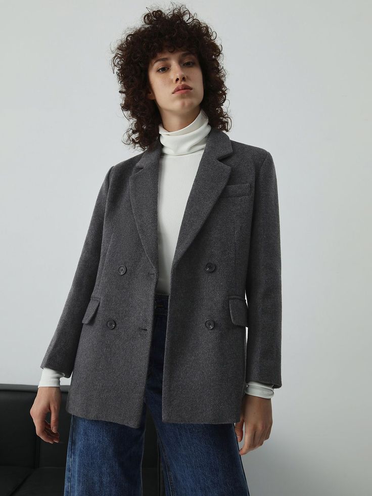 Woman with curly hair wearing a gray blazer and white turtleneck