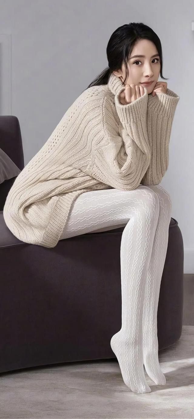 Woman in a beige turtleneck sweater and white patterned tights sitting indoors
