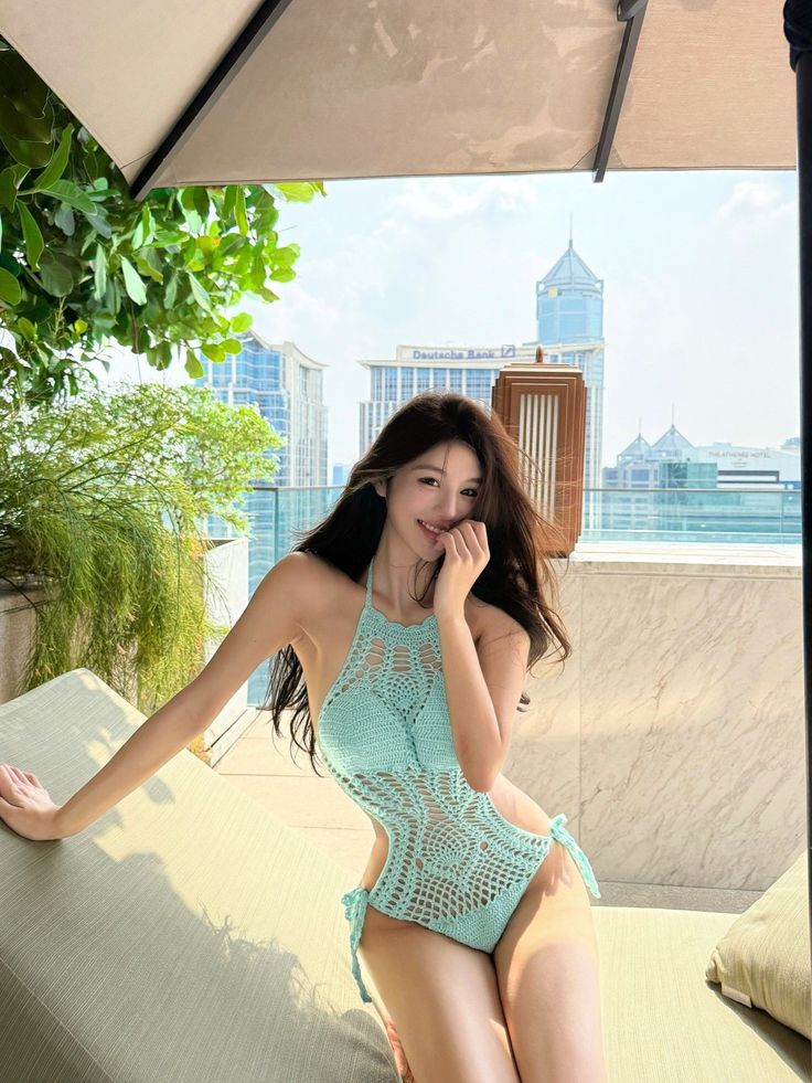 Woman in a light blue crochet swimsuit on a rooftop with a cityscape background