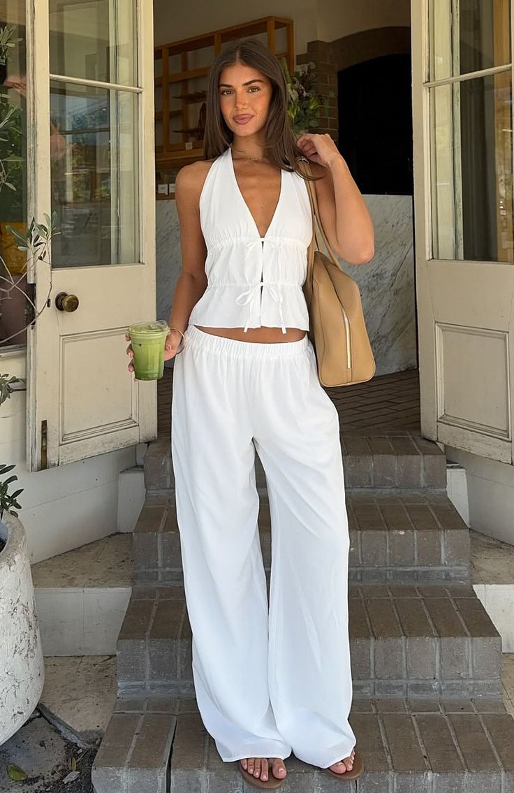 Woman in a white halter top and wide leg pants holding a green drink