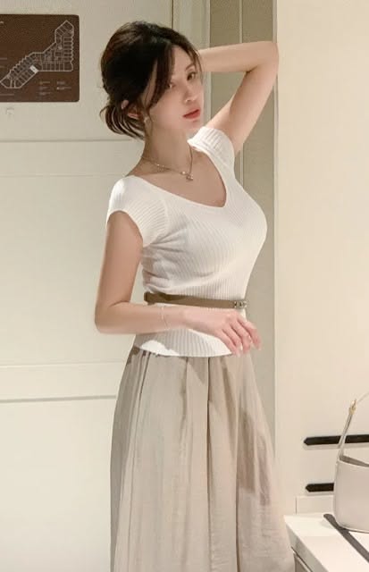 Woman with an updo wearing a white top and long skirt indoors
