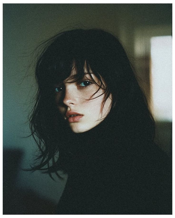 Woman with dark hair and a black turtleneck in soft indoor lighting