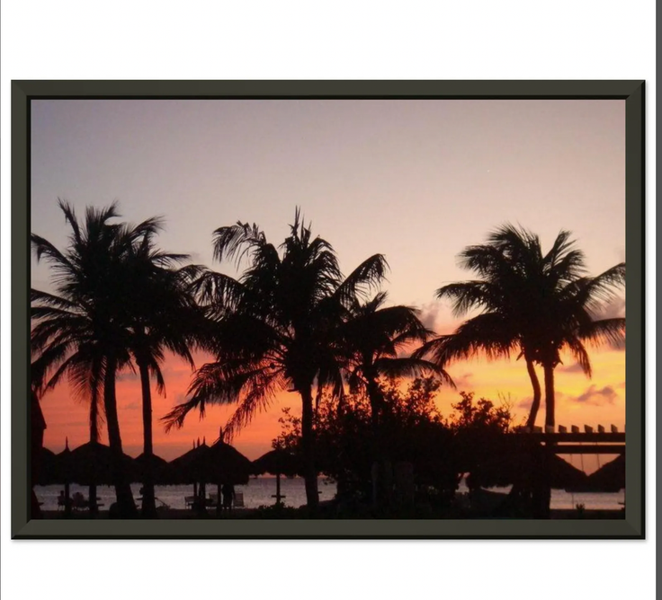 Palm trees and beach umbrellas silhouetted against a vibrant sunset sky