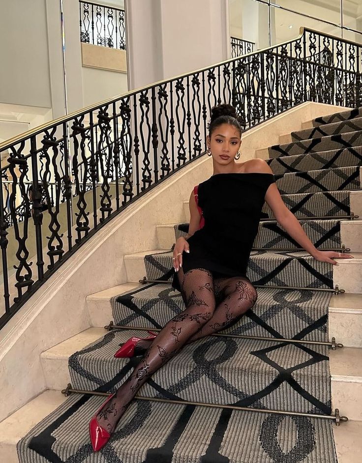 Woman in a black dress and fishnet stockings sitting on an ornate staircase