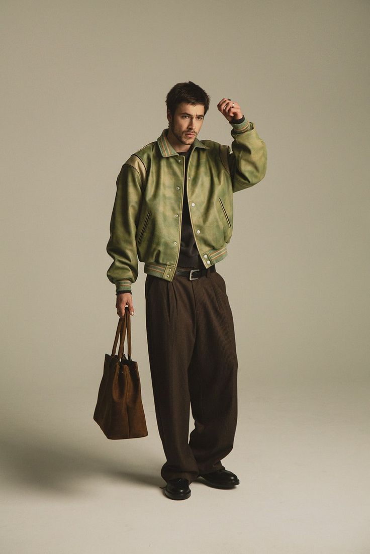 Man in a green bomber jacket and brown pants holding a suede bag