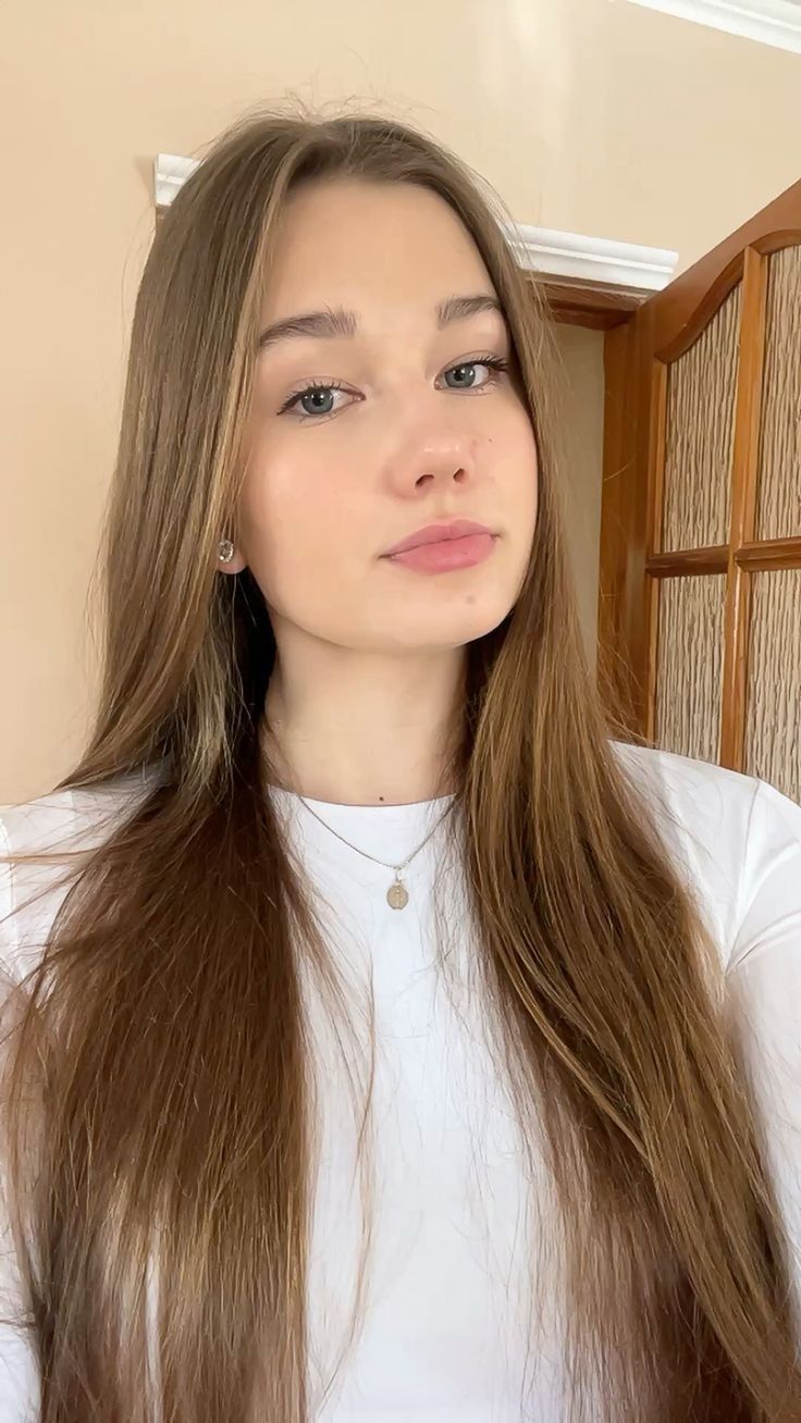 Young woman with long brown hair wearing a white shirt and necklace indoors