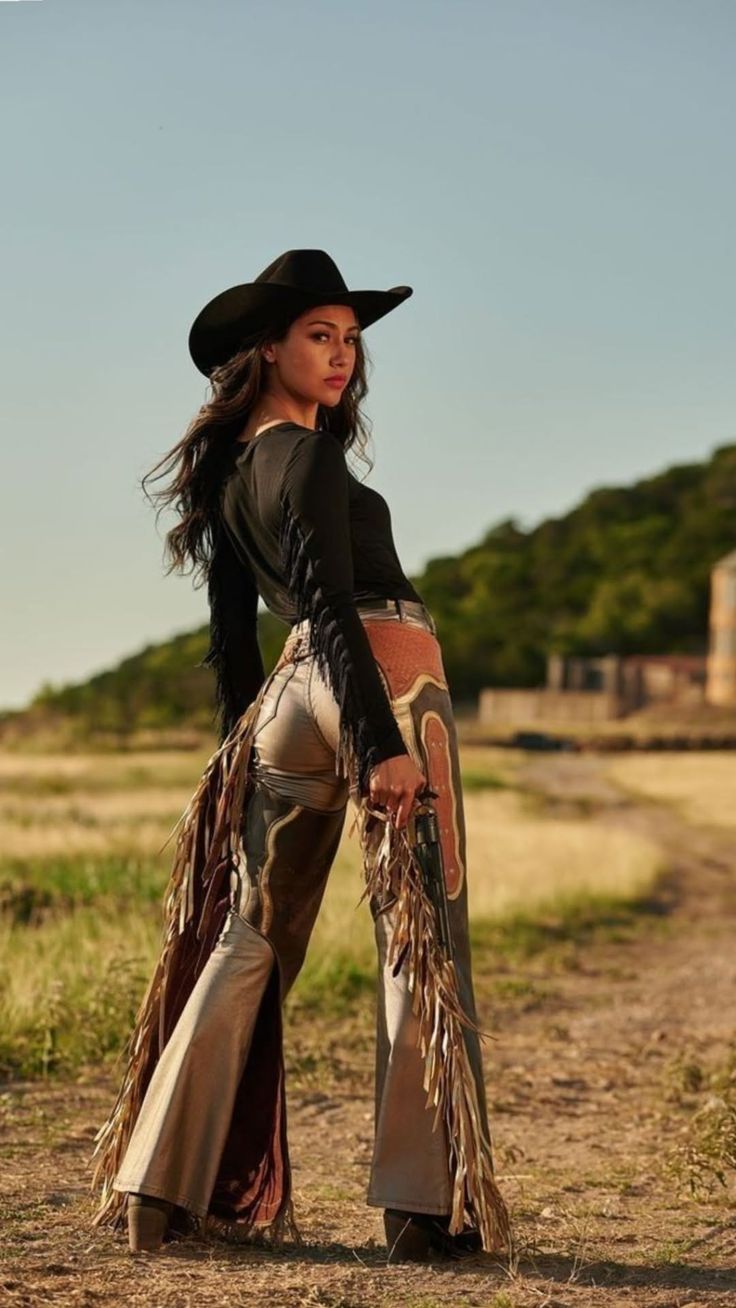 Woman in a cowboy hat and chaps looking over her shoulder in an outdoor setting