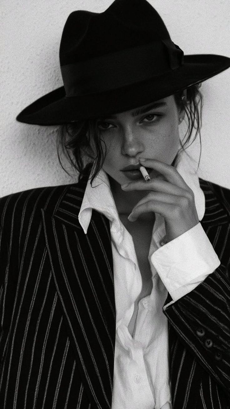 Woman in a fedora hat and pinstripe jacket smoking a cigarette