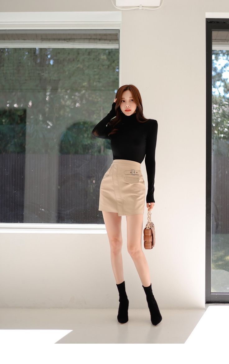 Woman in a black turtleneck and beige mini skirt posing indoors