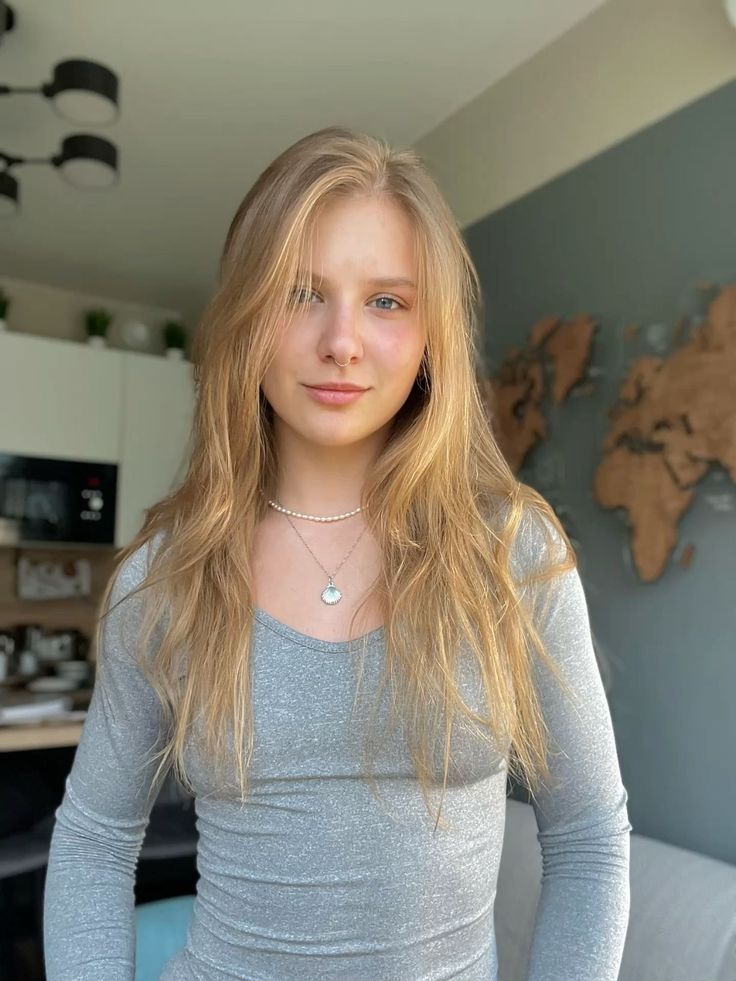 Young woman with long blonde hair wearing a gray top and necklaces indoors