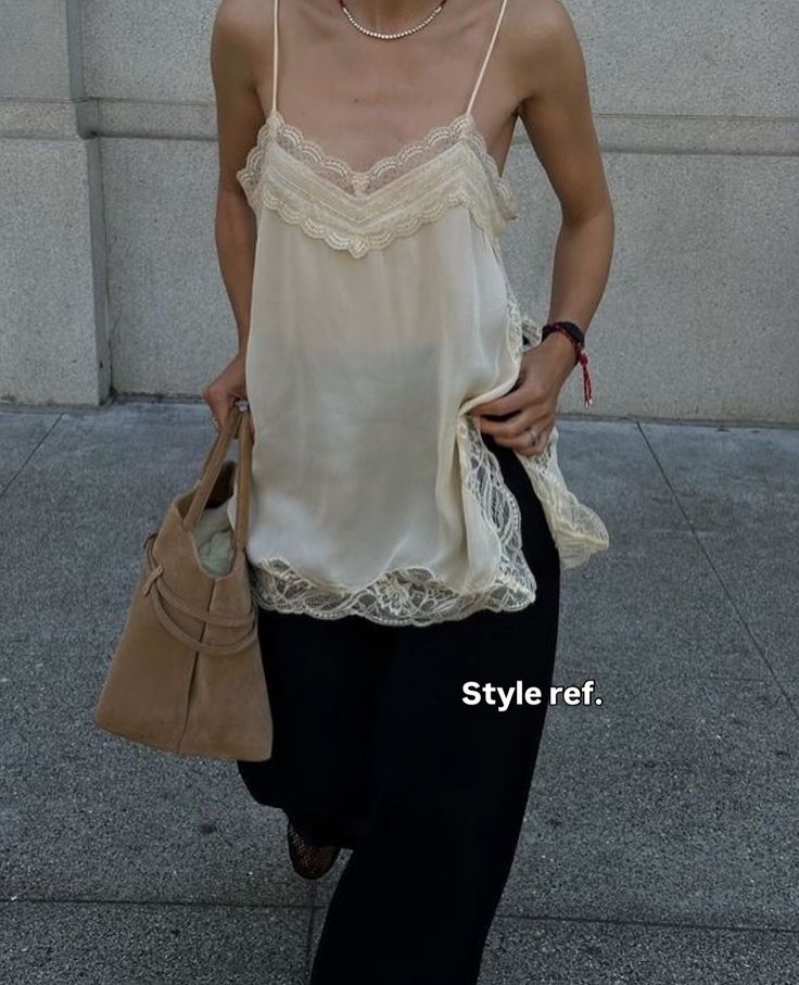Person in a lace camisole and black pants holding a suede bag outdoors