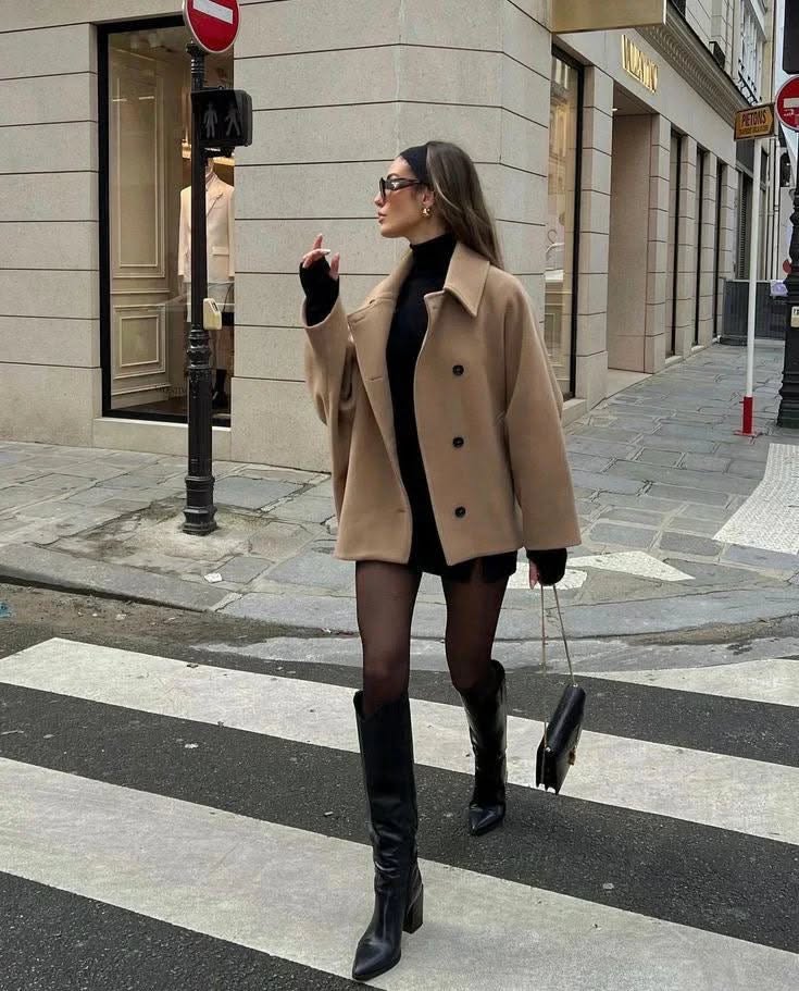 Woman in a camel coat and black dress crossing a city street