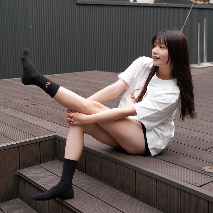 Woman with long hair sitting on wooden steps in a white t-shirt and black shorts