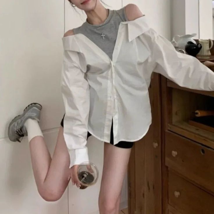 Woman in an off-shoulder white shirt and black shorts holding a drink