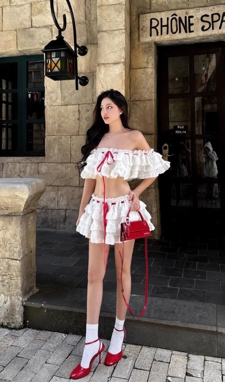 Woman in a white ruffled top and mini skirt with red heels and handbag